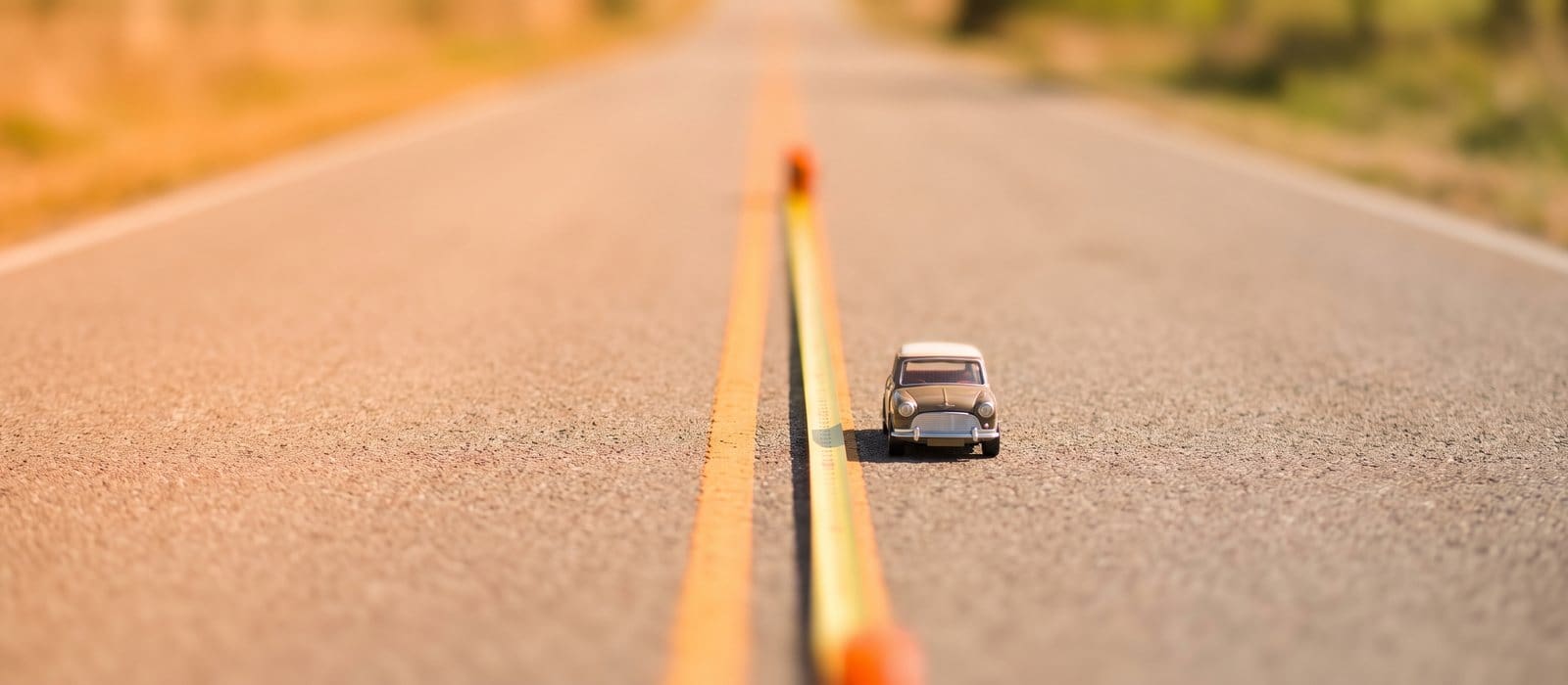 Tilt-shift view of a single car on a two-lane road with a measuring tape laid along the lane line
