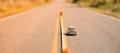 Tilt-shift view of a single car on a two-lane road with a measuring tape laid along the lane line