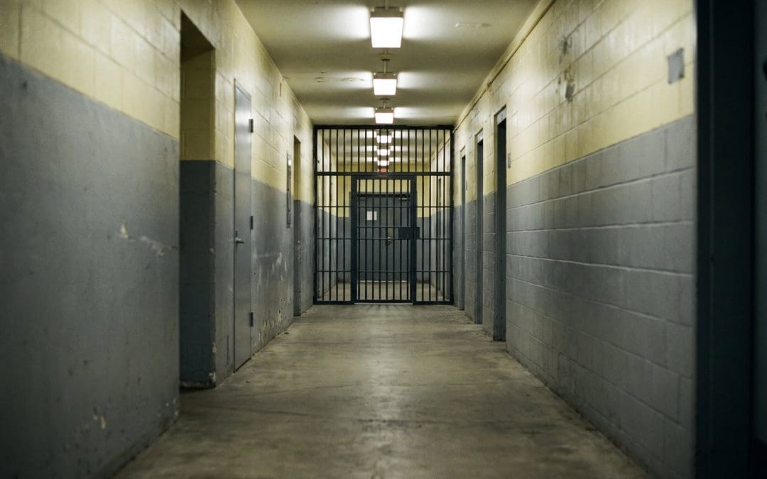 Long empty corridor in a correctional facility with a barred gate at the far end