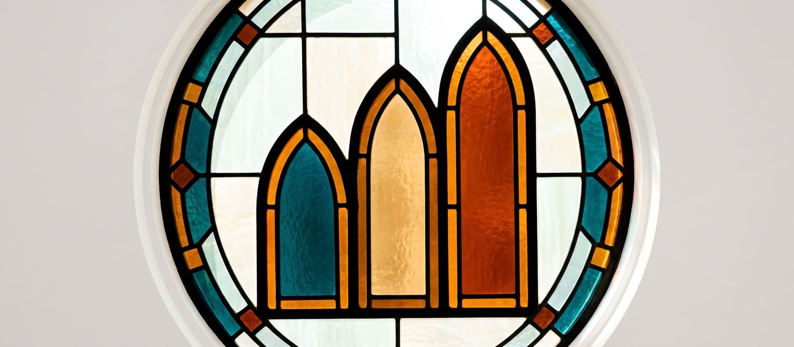 Stained-glass rondel of three pointed arch windows rising in height, teal, amber and burnt orange