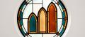 Stained-glass rondel of three pointed arch windows rising in height, teal, amber and burnt orange