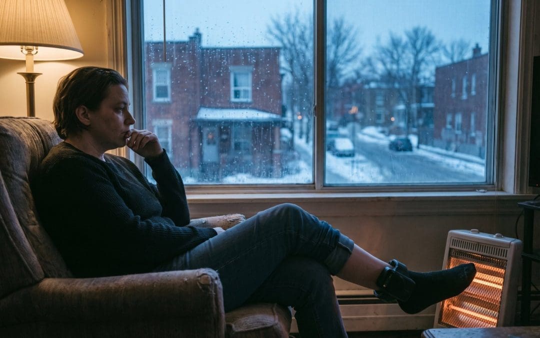Person sitting in an armchair by a window at home on a winter afternoon, looking out at the street