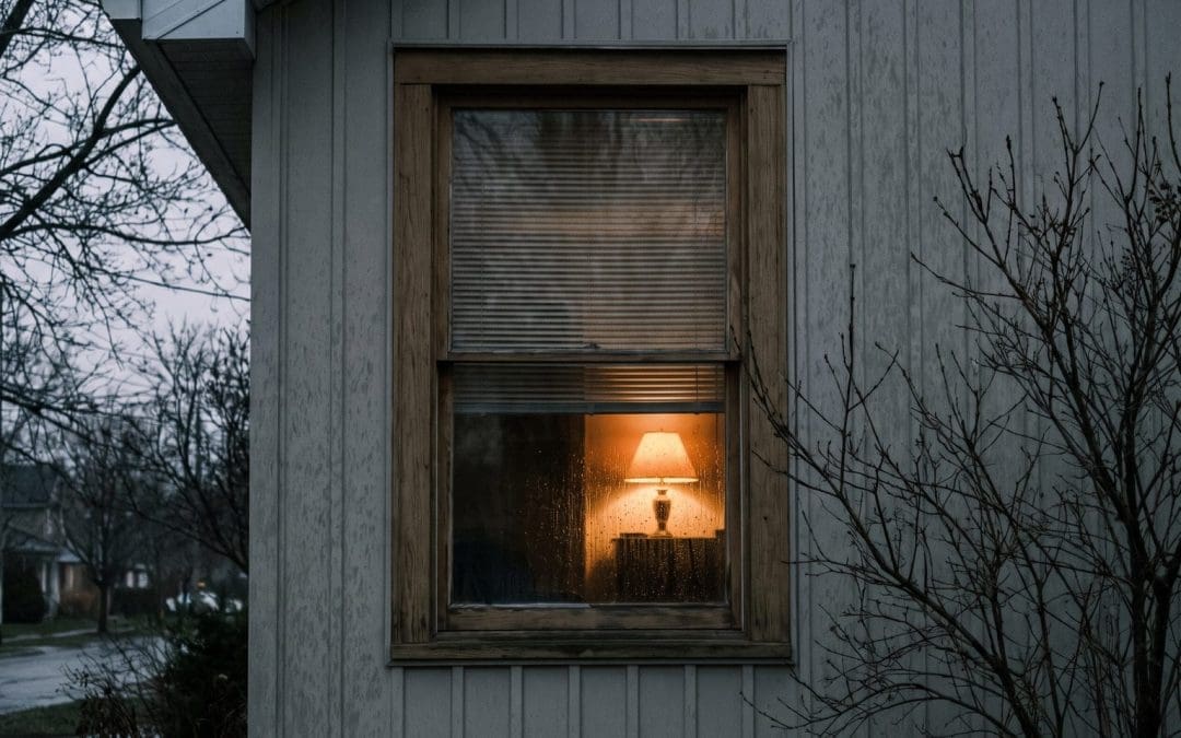 Residential window at dusk seen from outside with venetian blinds half closed and warm light within