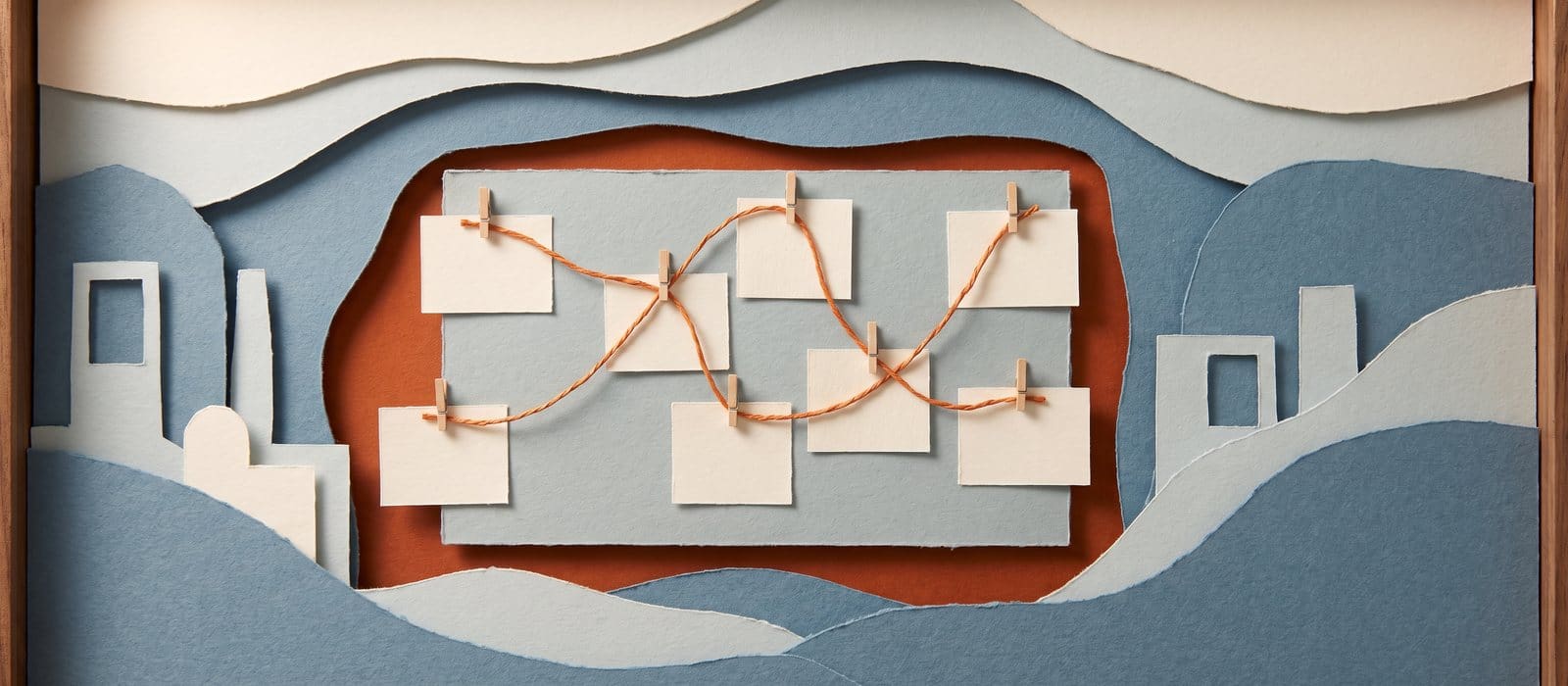 Cut-paper diorama of a strategy board with blank cards linked by orange thread