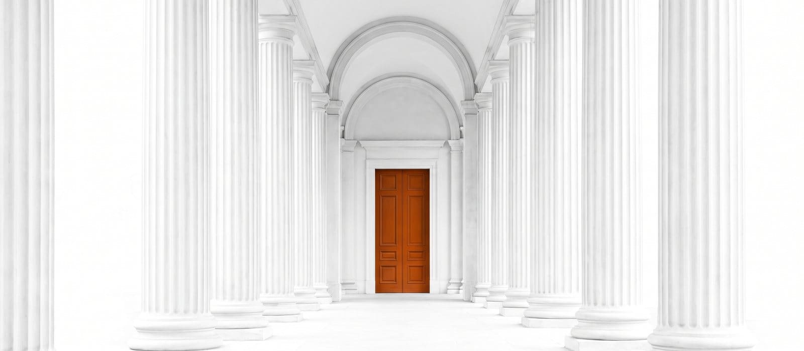 A bright white colonnade of classical columns leading to a single burnt-orange door