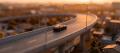 Tilt-shift view of a black sports coupe on an elevated expressway at golden hour