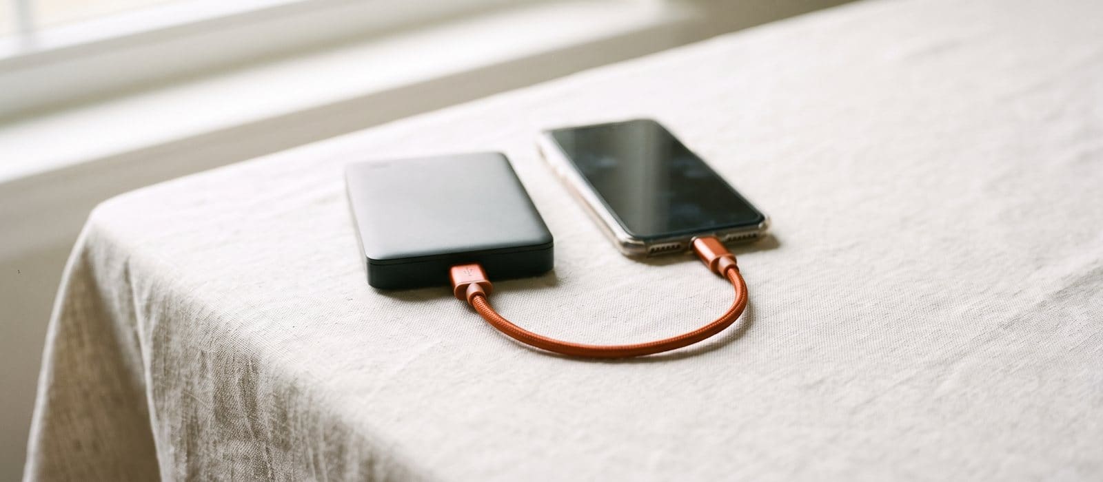 A phone connected by an orange cable to a small external drive on a linen tablecloth, being backed up