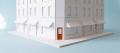 White card architectural model of a city street corner of shops with one burnt-orange shopfront door, on a pale blue backdrop