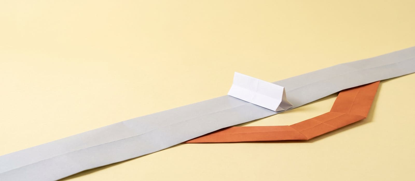 A folded paper road blocked by a small white barrier with a burnt-orange detour around it, on a pale yellow backdrop, representing defences to an obstruction charge