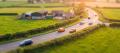 Tilt-shift view of a winding country highway through green farmland with a few small cars