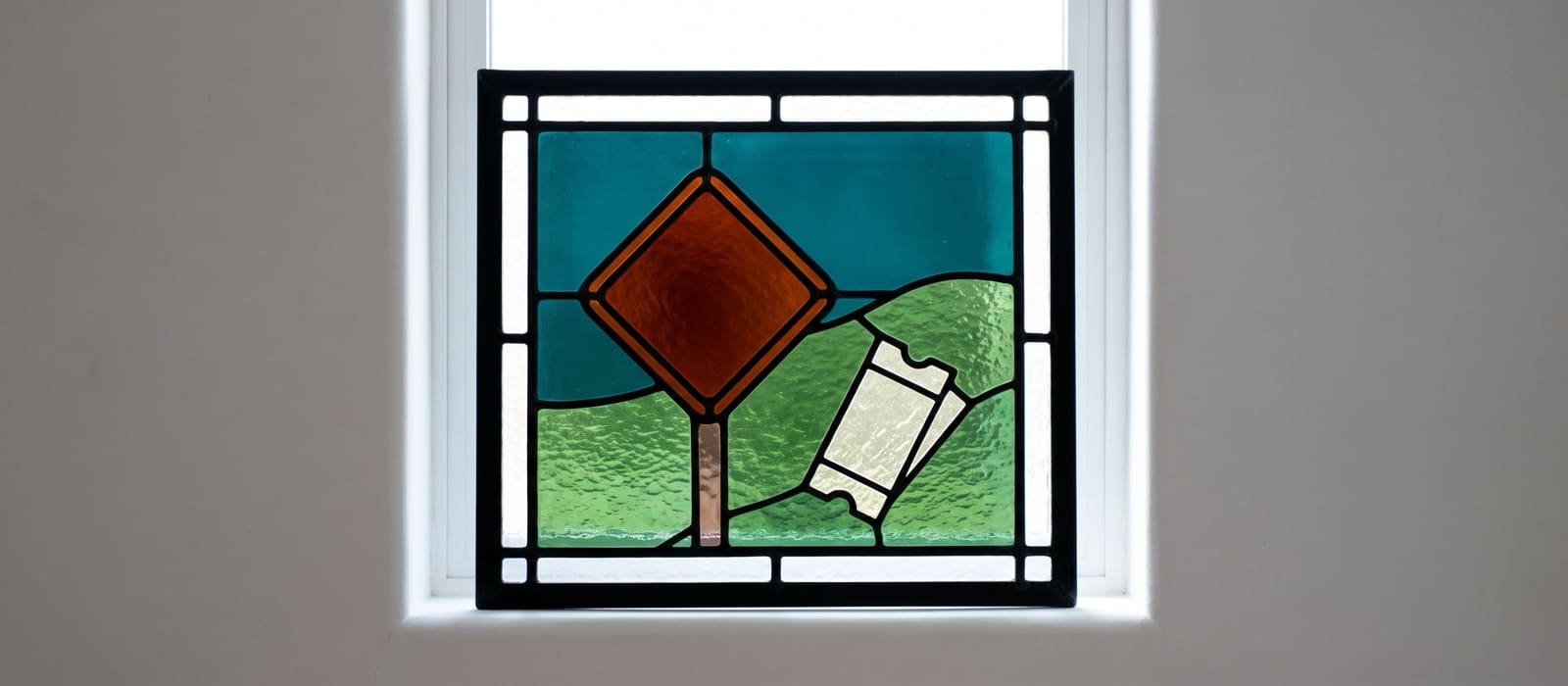Stained-glass window of an orange diamond road sign and a pale paper ticket against a teal sky and green hills