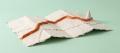 A handmade papier-mache folded road map with a raised burnt-orange route running across it and a small map pin, on a pale mint background, representing an importing or transport route