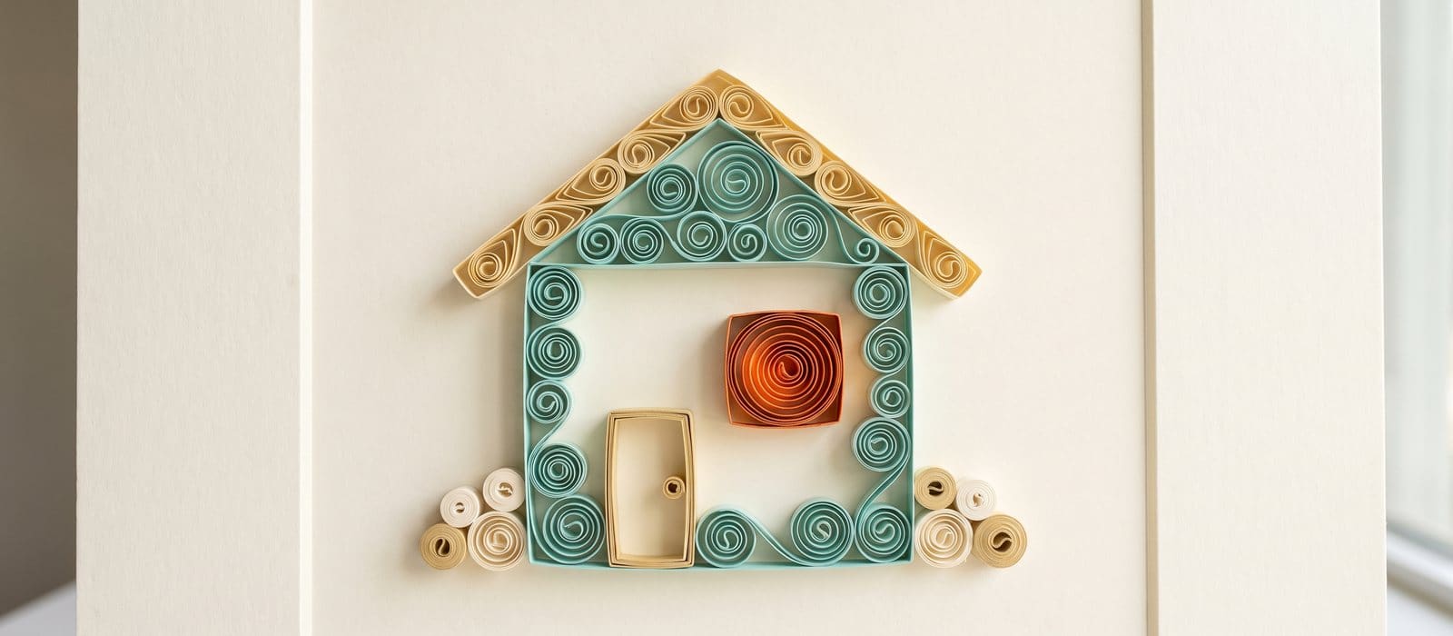 Paper quilling of a teal and gold paper house with one window glowing in burnt orange