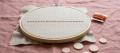 Wooden embroidery hoop holding linen with one straight line of burnt-orange running stitches, on dusty-rose linen