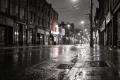 Wide empty downtown side street at night in the rain with light reflecting on wet asphalt