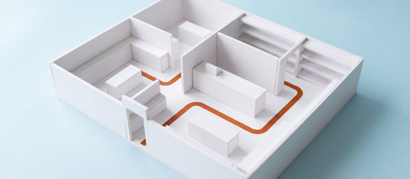 White foam-board floor plan model of a small shop with an orange route line traced from the entrance to the counter