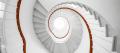 Looking up a bright white spiral staircase toward a skylight, its single handrail picked out in burnt orange