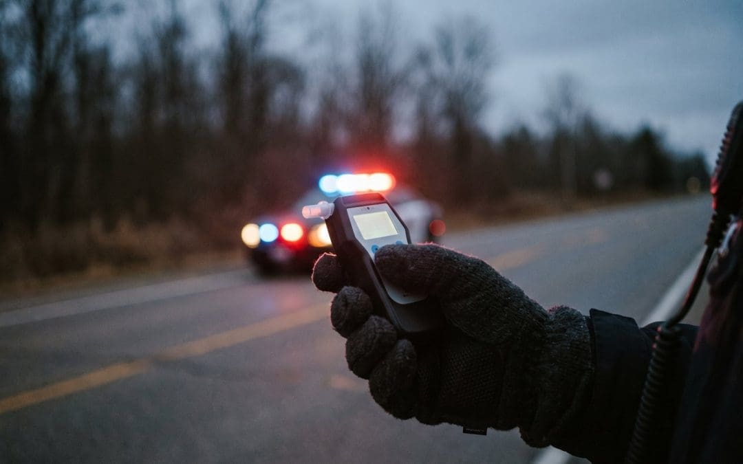 Police officer gloved hand holding a roadside screening device at a traffic stop at dusk
